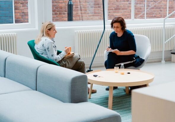two woman sits on sofa chairs inside house